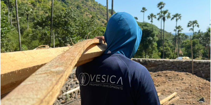 Builder carrying timber with Vesica Property Developments t-shirt on