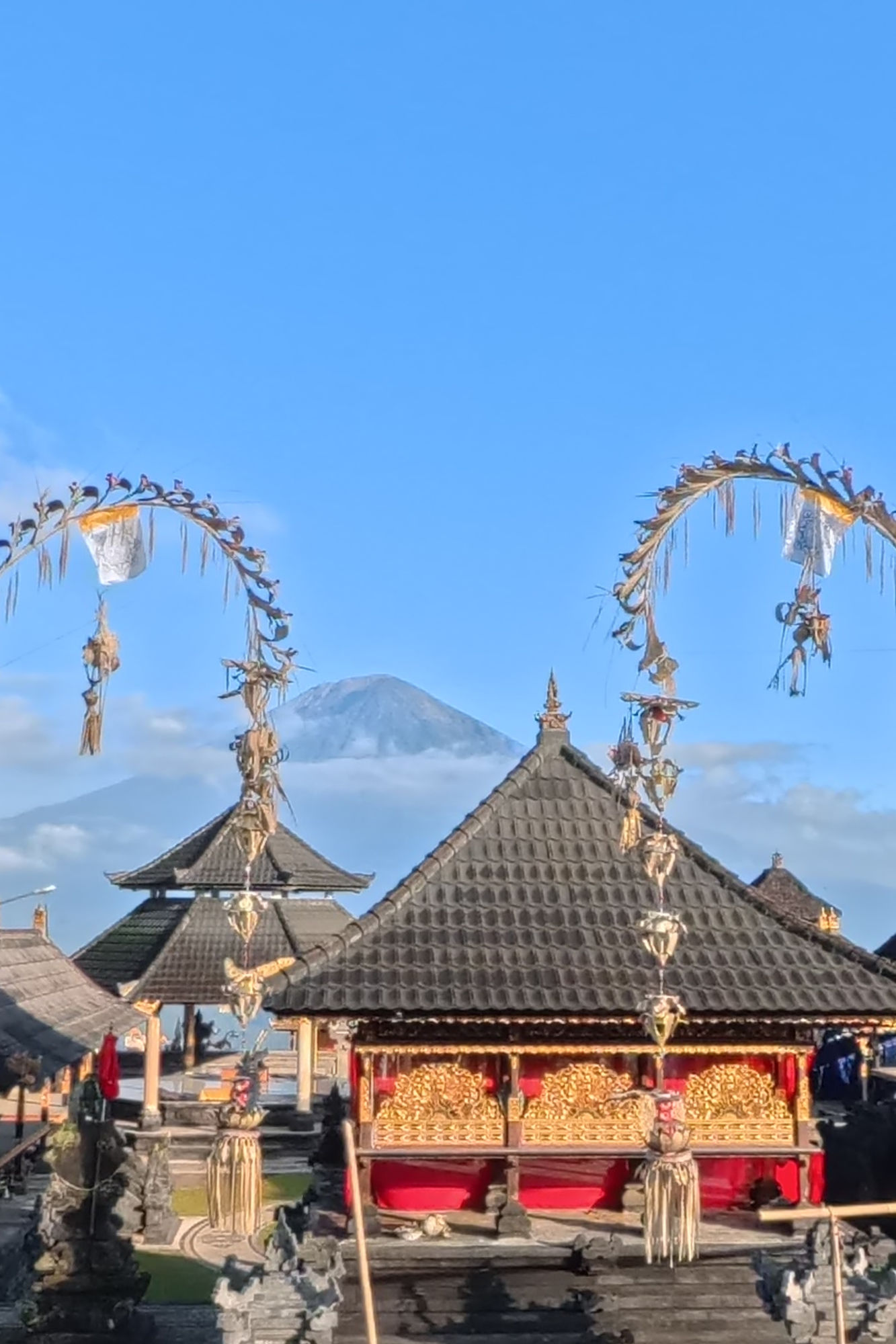 Pura Lempuyang and Mount Agung – Temple Experiences near Amed Pura Lempuyang temple pavilions with red and gold carved panels beneath bamboo penjor, with Mount Agung rising behind, in East Bali near Vesica Villas Resort in Amed.