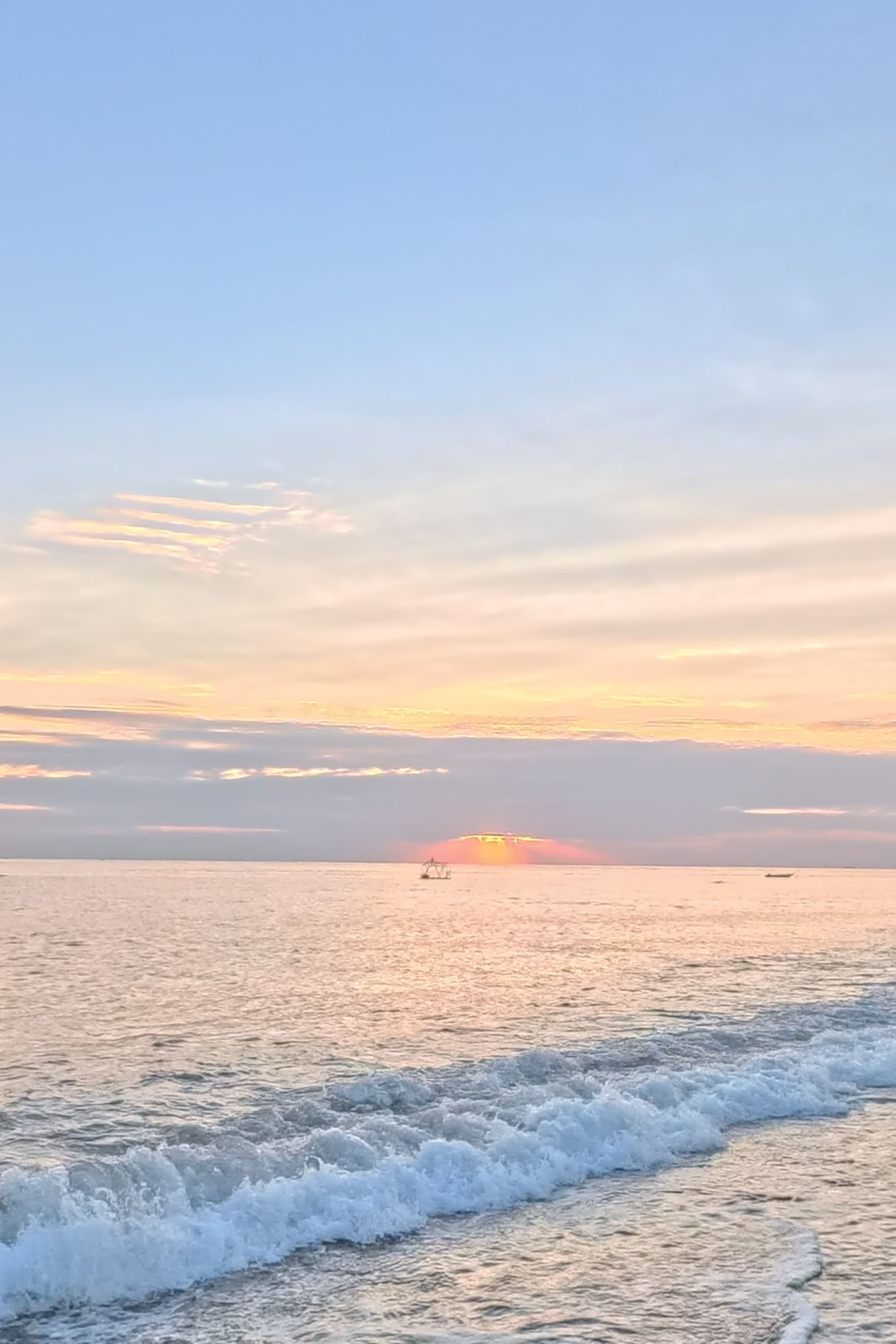 Sunrise over the Bali Sea – Amed Beach, East Bali Sunrise over the calm Bali Sea from the shore at Amed, with fishing boats on the horizon and gentle waves breaking on the beach near Vesica Villas Resort