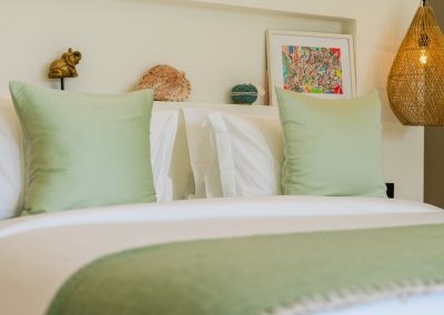 Bed with white linens and sage accents under a niche with shell and art, woven pendant glowing at Angin Laut at Vesica Villas Resort in Amed
