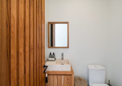 Powder bathroom at Angin Laut at Vesica Villas Resort in Amed, seen through an open wood-slat door, with a stone vessel sink, wood vanity, and white toilet