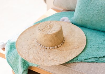 Wide-brim straw hat with a cowrie-shell band resting on a textured teal throw at Angin Laut at Vesica Villas Resort in Amed