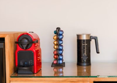 Red capsule espresso machine, wire pod rack, and black milk frother on a glass wood counter at Angin Laut at Vesica Villas Resort in Amed