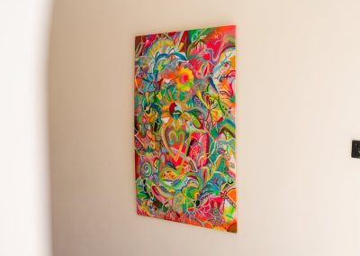 Tall colorful abstract painting on a cream wall beside a black light switch at Angin Laut at Vesica Villas Resort in Amed