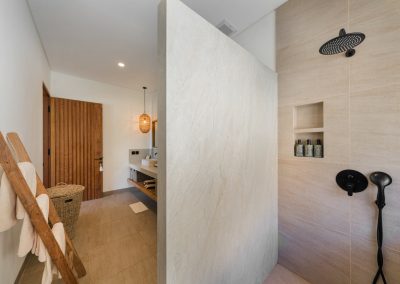 Walk-in shower with matte black rain head and niches beside a wood towel ladder at Angin Laut at Vesica Villas Resort in Amed