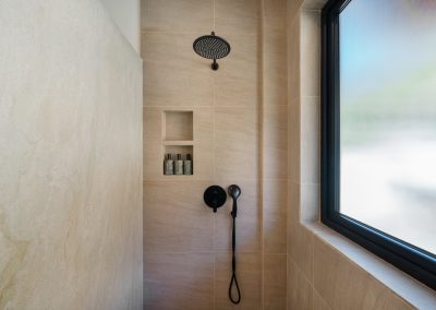 Walk-in shower at Angin Laut at Vesica Villas Resort in Amed, with matte black rain head, handheld wand, tiled niche, and frosted window