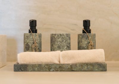 Close-up of green-speckled stone dispensers, cup, and rolled towels on a stone tray at Angin Laut at Vesica Villas Resort in Amed