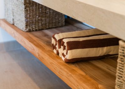Brown-and-cream striped towels and woven baskets on the wood shelf under a bathroom vanity at Angin Laut at Vesica Villas Resort in Amed