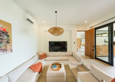 Sunken living lounge at Angin Laut at Vesica Villas Resort in Amed, with cream sectional, woven rattan pendant, recessed TV, and black-framed glass doors to the terrace