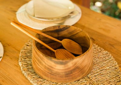 Close-up of a wooden serving bowl with wooden spoons on a woven mat at Angin Laut dining table at Vesica Villas Resort in Amed