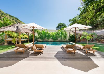 Private turquoise pool at Angin Laut at Vesica Villas Resort in Amed, with timber deck, four loungers, white umbrellas, thatched bale, and hillside beyond