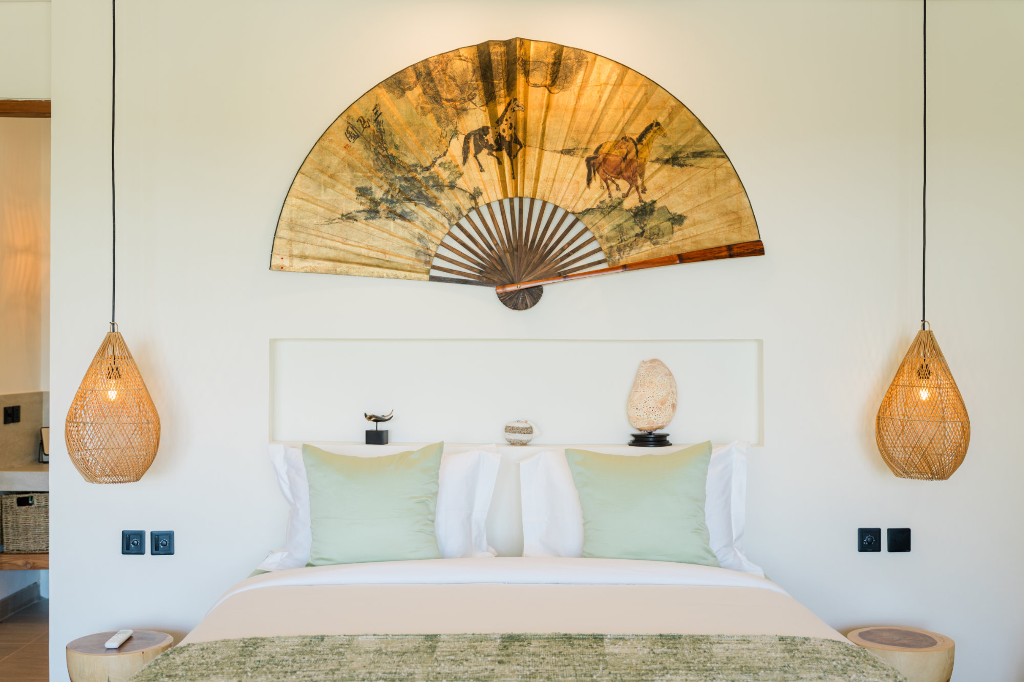 Angin Laut Master Bedroom Sun-beds with umbrella facing a turquoise pool in a luxury residence at the Vesica Villas Resort in Amed. A traditional bale day-bed with alang-alang roof sites at the end of the pool and tropical hills are visible in the background.