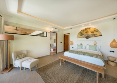 King bedroom at Angin Laut at Vesica Villas Resort in Amed, with sage bedding, rattan pendants, fan wall art, wooden bench, and cream armchair seating nook