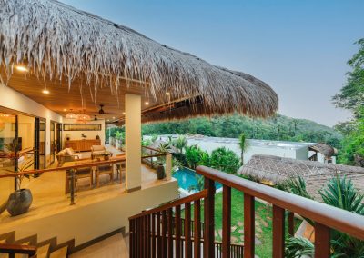 Open-air thatched living and dining terrace at Angin Laut villa at Vesica Villas Resort in Amed, at dusk, with warm lighting overlooking the pool and tropical hillside
