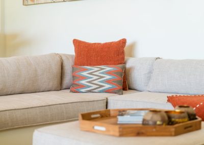 Beige sofa with orange and chevron pillows and a wooden tray of books on the ottoman at Angin Laut at Vesica Villas Resort in Amed