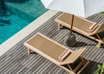 Two wood sun loungers with striped towels on a grey deck beside the turquoise pool at Angin Laut at Vesica Villas Resort in Amed