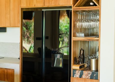 Black refrigerator in wood cabinetry beside a wine glass rack and cocktail bar shelf at Angin Laut at Vesica Villas Resort in Amed