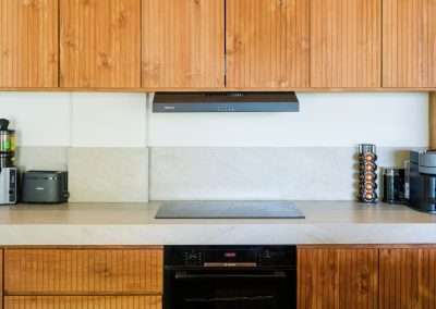 Kitchen cooktop with built-in oven, range hood, toaster, and coffee machines along ribbed wood cabinets at Angin Laut at Vesica Villas Resort in Amed