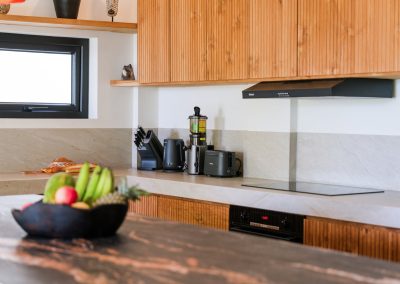 Modern kitchen at Angin Laut at Vesica Villas Resort in Amed, with light wood slatted cabinets, black countertop appliances, cooktop, and a fruit bowl on the island