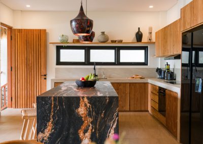 Kitchen at Angin Laut at Vesica Villas Resort in Amed, with a black and orange veined stone island, wooden bar stools, slatted cabinets, and a black refrigerator