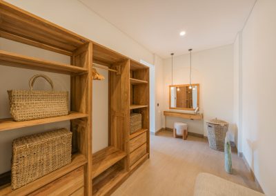 Walk-in closet at Angin Laut at Vesica Villas Resort in Amed, with a light-wood open wardrobe, woven baskets, and a vanity with pendant lights at the far wall
