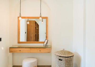 Wooden floating vanity at Angin Laut at Vesica Villas Resort in Amed, with a square mirror, Edison pendant lights, upholstered stool, and woven laundry basket