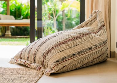 Patterned fringed bean bag on tiled floor by curtains and a glass door to a garden bale at Angin Laut at Vesica Villas Resort in Amed