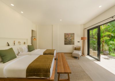 Twin bedroom with green runners, wooden bench, corner armchair, and open garden doors at Angin Laut at Vesica Villas Resort in Amed