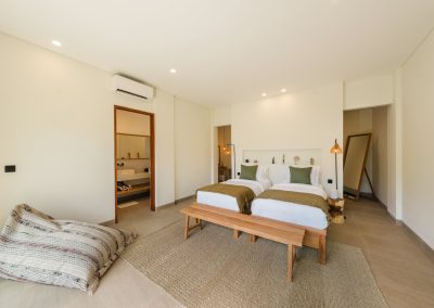 Twin beds with olive accents, patterned bean bag, and wood bedside table at Angin Laut at Vesica Villas Resort in Amed