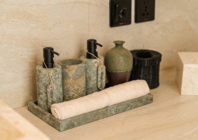 Stone tray with moisturizer and hand-wash dispensers, rolled towel, and green vase on the vanity at Angin Laut at Vesica Villas Resort in Amed