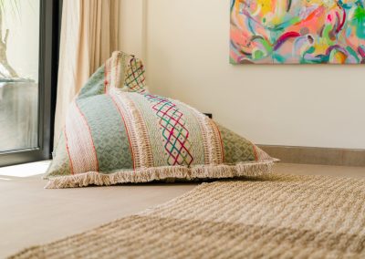 Patterned fringed bean bag on light tiles by a glass door and colorful abstract art at Angin Laut at Vesica Villas Resort in Amed