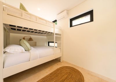 Bunk room at Villa Svara with a white wooden bunk bed, sage green pillows, cone rattan reading light, marble-tiled floor, oval jute rug, and small black-framed windows