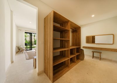 Dressing room at Villa Svara at Vesica Villas Resort in Amed, with an open wood wardrobe, floating vanity and stool, woven basket, and marble floors opening towards tropical greenery