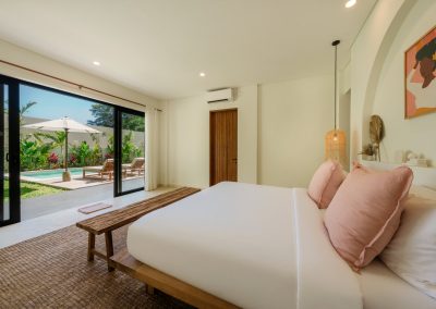 King bedroom at Villa Svara at Vesica Villas Resort in Amed, opening through black-framed glass doors to a private pool with wood loungers, a white umbrella, and tropical greenery
