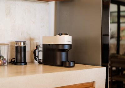 Coffee corner at Villa Svara with a black-and-white Nespresso machine, milk frother, capsule jar, and marble-tile backsplash beside the refrigerator