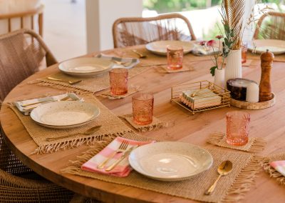 Dining table at Villa Svara at Vesica Villas Resort in Amed, set with fringed jute placemats, speckled plates, gold cutlery, pink checkered napkins, and pink embossed glassware