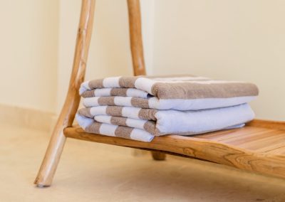 Folded striped pool towels stacked on a light wood branch-leg shelf over marble tiles at Villa Svara.