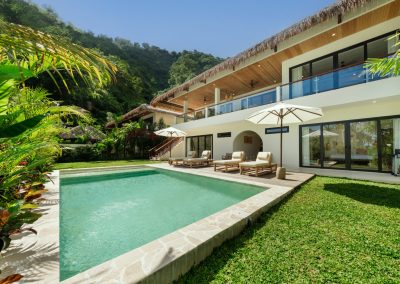 Wide view of Villa Svara’s pool, wooden deck, and two-storey thatched villa against Amed’s green hillside.