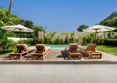 Marble terrace leading to a wooden sun deck and private pool at Villa Svara beneath a clear Amed sky.