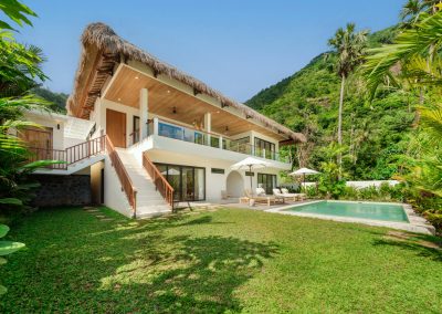 Two-storey thatched Villa Svara at Vesica Villas Resort in Amed with external stairs, private pool, and forested hillside backdrop.